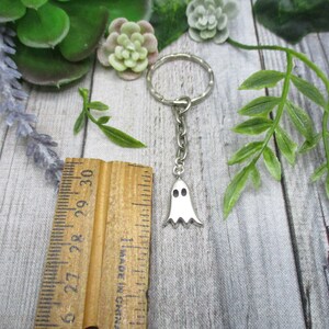 May include: A silver ghost keychain with a silver key ring. The ghost has two black eyes and a white body.