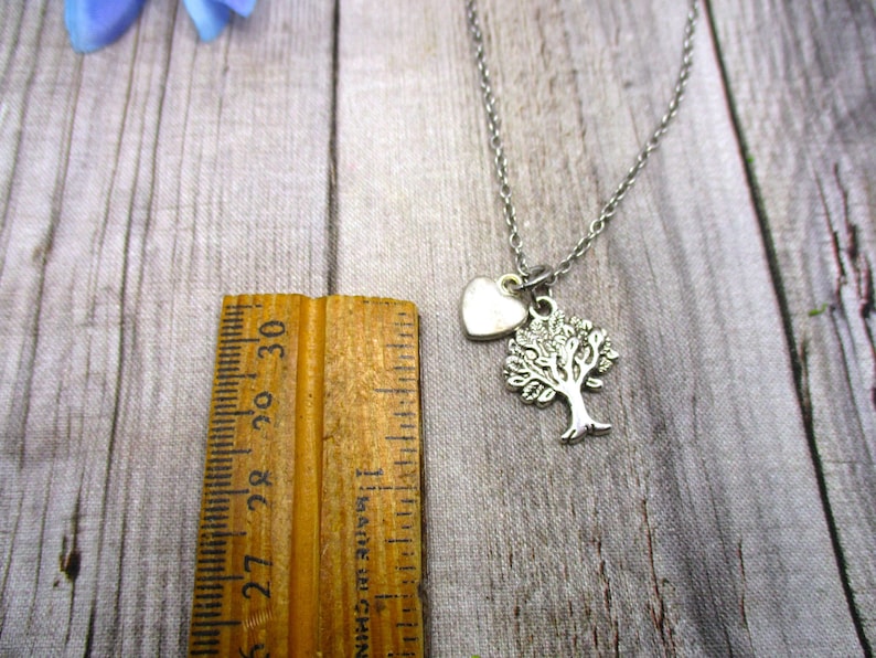 Puede incluir: Un collar de plata con un dije de &aacute;rbol y coraz&oacute;n. El collar est&aacute; sobre una superficie de madera con una regla para referencia de tama&ntilde;o.