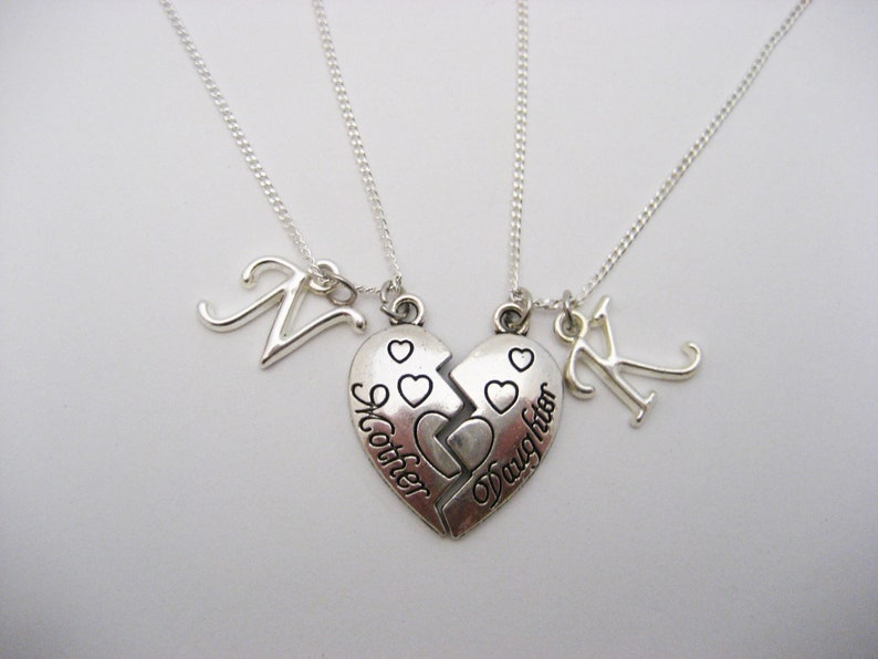 May include: Two silver necklaces with matching heart pendants that say "Mother" and "Daughter". Each necklace also has a silver letter charm, one with the letter "N" and the other with the letter "K".