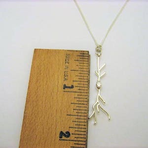 Puede incluir: Un collar de plata con un delicado colgante de rama. El colgante presenta una peque&ntilde;a piedra transparente en el centro de la rama. El collar mide aproximadamente 2,5 cm de largo.