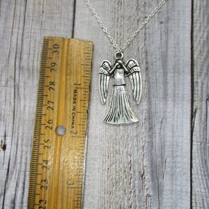 May include: Silver necklace with a Weeping Angel pendant. The pendant is about 2 inches tall and features a detailed design of the angel with outstretched wings.