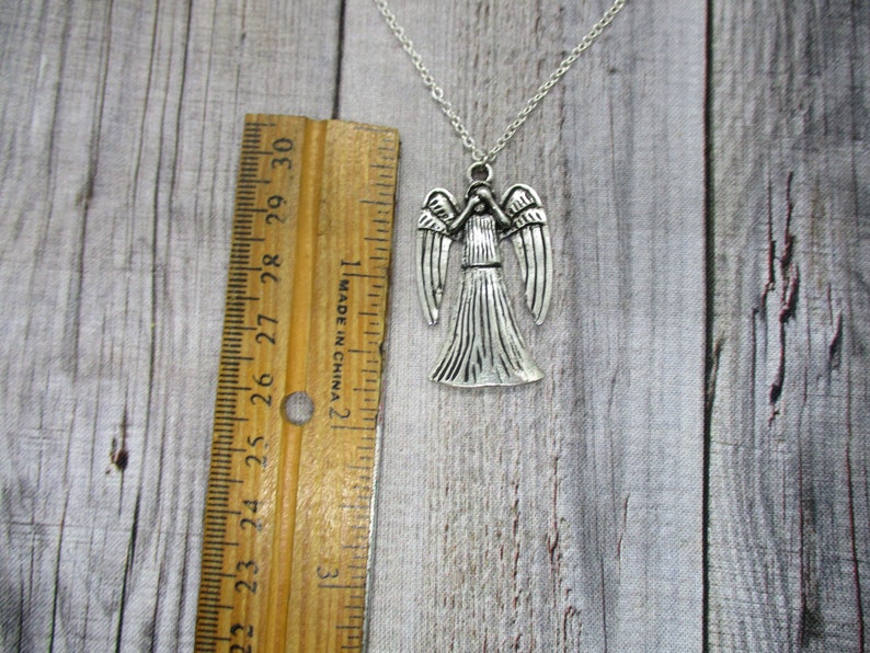 May include: Silver necklace with a Weeping Angel pendant. The pendant is about 2 inches tall and features a detailed design of the angel with outstretched wings.