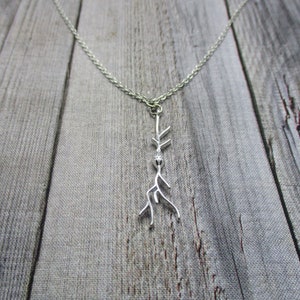 Puede incluir: Un collar de plata con un delicado colgante de rama. La rama est&aacute; estilizada y tiene una peque&ntilde;a cuenta en la parte superior.