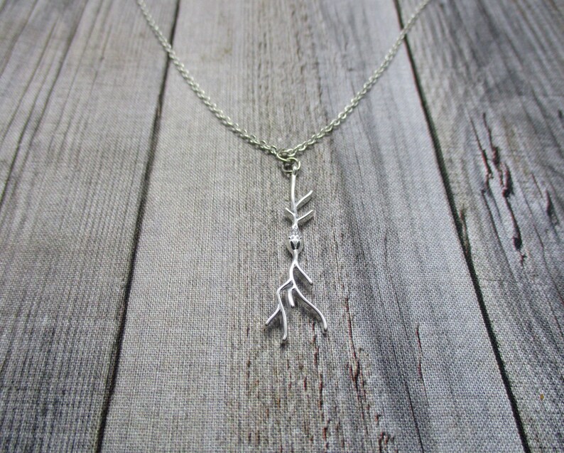 Puede incluir: Un collar de plata con un delicado colgante de rama. La rama est&aacute; estilizada y tiene una peque&ntilde;a cuenta en la parte superior.