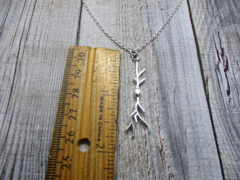 Puede incluir: Collar de plata con un delicado colgante de rama. El colgante mide aproximadamente 5 cm de largo y presenta un peque&ntilde;o cristal transparente.