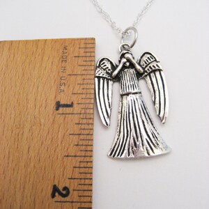 May include: Silver necklace with a pendant of a weeping angel from the Doctor Who television series. The pendant is about 2 inches tall and is shown next to a ruler.