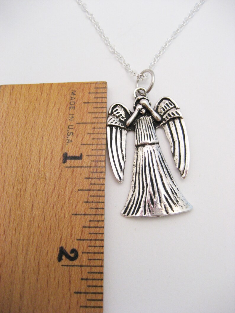 May include: Silver necklace with a pendant of a weeping angel from the Doctor Who television series. The pendant is about 2 inches tall and is shown next to a ruler.