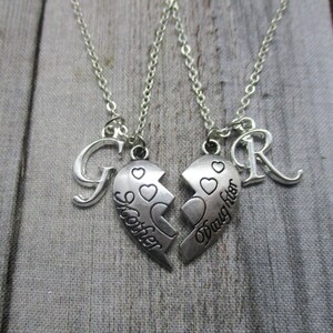 May include: Two silver necklaces with matching broken heart pendants. One pendant says "Sister" and the other says "Daughter". Each necklace has a letter charm, one is a "G" and the other is an "R".