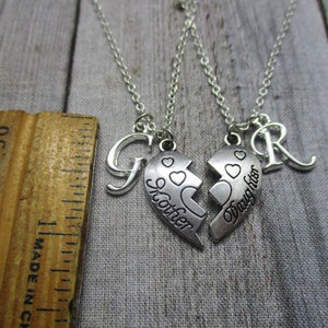 May include: Two silver necklaces with matching heart pendants that say "Mother" and "Daughter". The necklaces also have a letter "G" and a letter "R" charm.