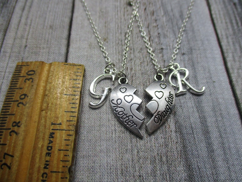 May include: Two silver necklaces with matching heart pendants that say "Mother" and "Daughter". The necklaces also have a letter "G" and a letter "R" charm.