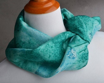 May include: A teal blue silk scarf with a marbled pattern. The scarf is folded and draped around a mannequin's neck.