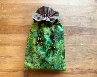 May include: A green drawstring bag with a forest pattern. The bag has a brown satin lining and a drawstring closure with decorative beads. The bag is approximately 18 cm tall and 13 cm wide.
