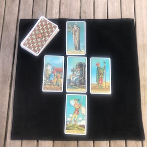 May include: Tarot card reading spread on a black felt cloth. The cards are laid out in a cross shape. The cards are: The Hermit, Queen of Cups, Page of Wands, Page of Swords, and a face-down card.