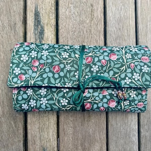 May include: A green fabric pouch with a floral pattern and a green drawstring closure. The pouch is closed and sitting on a wooden surface.