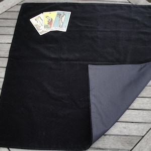 May include: Black velvet tarot cloth with a grey underside. The cloth is folded in half and three tarot cards are placed on top of the cloth.