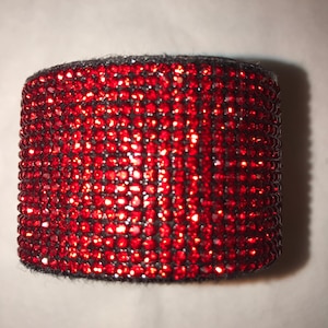 May include: A red rhinestone-covered bracelet with a black fabric base.