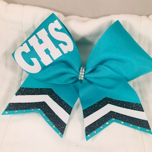 May include: A teal cheerleading hair bow made of grosgrain ribbon featuring the white glittered letters CHS on one loop. The tails are decorated with black and white glittered chevron stripes and small clear rhinestones along the bottom edges.