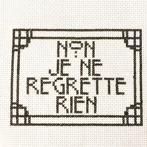 Op de afbeelding: Zwart-witte kruissteekborduurwerk met een ingelijst ontwerp met de tekst "Non je ne regrette rien".