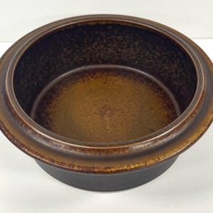 May include: A brown ceramic bowl with a textured, speckled glaze. The bowl has a wide rim and a rounded bottom.