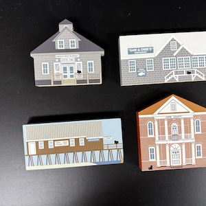 May include: Four wooden building-shaped magnets. One is grey with a sign that reads "OWENS RESTAURANT EST. 1986". Another is a rectangular building with "SAM & OMI'S" on the sign. The other two are a pier and a brick building.