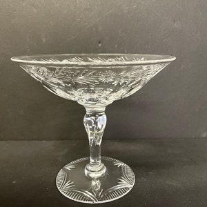 May include: A clear glass pedestal bowl with a cut glass design. The bowl has a wide, shallow base and a tall, slender stem.