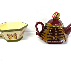 May include: A set of ceramic teacups and teapot with a butterfly design. The teapot is brown, red, and gold with a butterfly on the lid. The teacup is white with a green rim and a butterfly design.