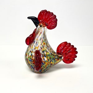 May include: A colorful glass rooster figurine with red, white, and yellow accents. The rooster has a red comb and wattle, and a black beak.