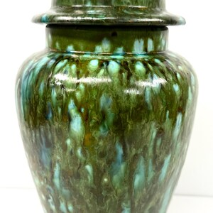 May include: A glazed ceramic jar with a lid. The jar is a deep green color with streaks of teal and brown. The lid has a small knob on top. The jar is a decorative item.