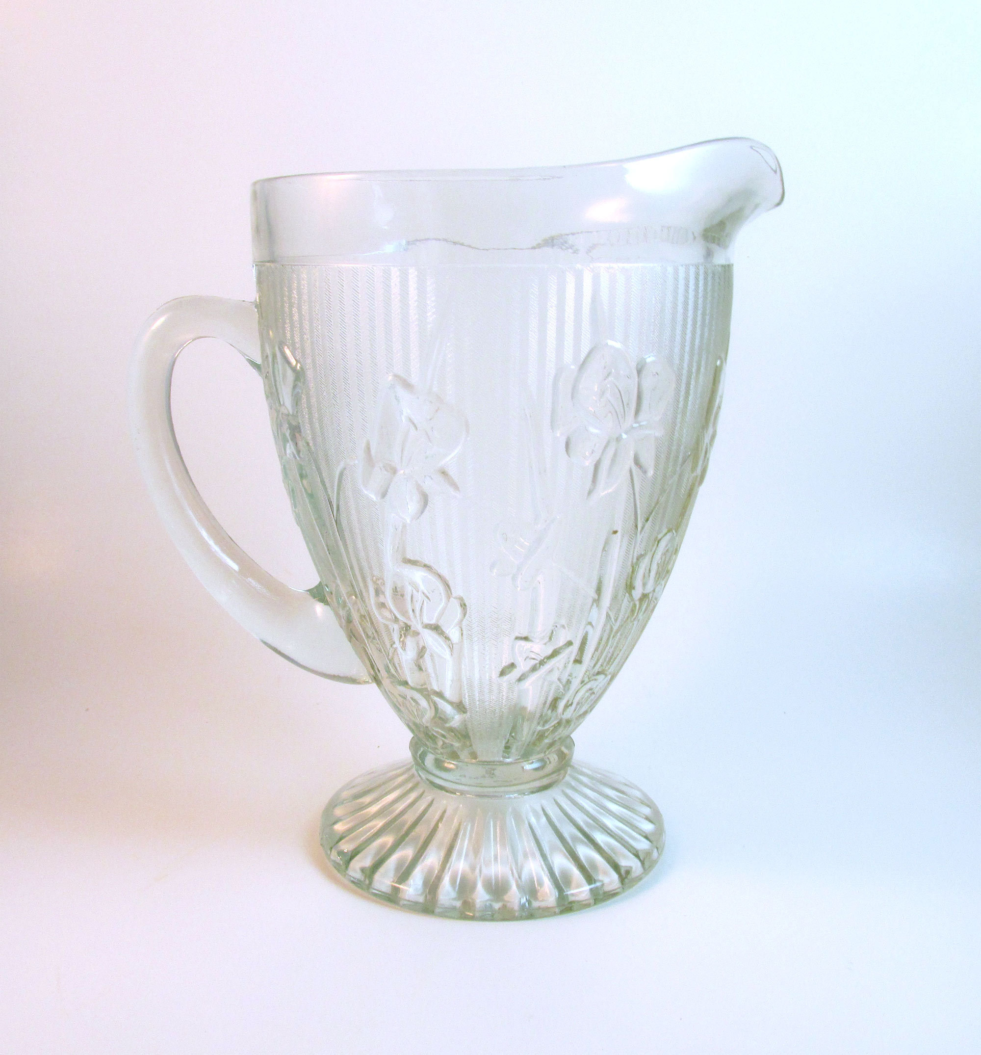 May include: A clear glass pitcher with a textured, ribbed design and a floral pattern. The pitcher has a wide mouth and a handle.