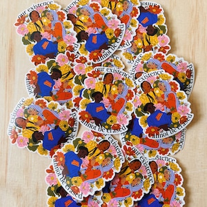 May include: A stack of colorful stickers with three women holding hands in a circle. The stickers have a floral design and the text "Our existence cannot be erased".