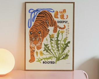 May include: A framed art print featuring an orange and black tiger walking above green dandelion plants with yellow flowers. The print includes a blue ribbon, orange stones, and the text DEEPLY ROOTED in black capital letters on a cream background.