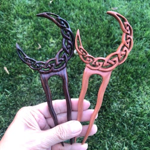 May include: Two wooden hair sticks with a crescent moon design. One stick is dark brown and the other is light brown.