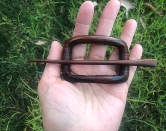 May include: A dark brown wooden hair slide featuring a rectangular frame with rounded corners and a matching pointed wooden stick that passes horizontally through the center of the frame to secure hair in place with a smooth polished finish.