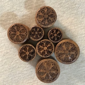 May include: Set of seven wooden ear gauges with intricate carved designs. The gauges are brown and feature a repeating geometric pattern.