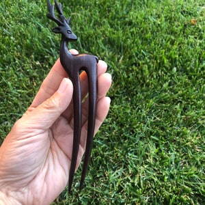 May include: A dark brown wooden hair fork featuring a deer silhouette. The deer has detailed antlers and a slender body. The fork has two long, smooth prongs. The hair accessory is designed for decorative hair styling.