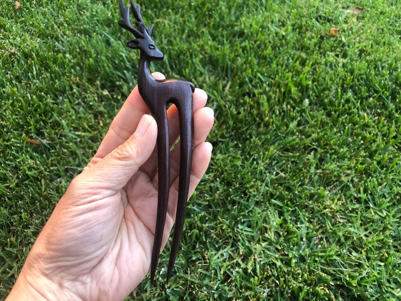 May include: A dark brown wooden hair fork featuring a deer silhouette. The deer has detailed antlers and a slender body. The fork has two long, smooth prongs. The hair accessory is designed for decorative hair styling.
