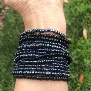 May include: A stack of black beaded bracelets on a person's wrist. The bracelets are made of small, round beads that are tightly woven together.