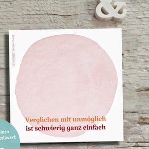 Könnte beinhalten: Eine quadratische weiße Karte mit einem großen, blassrosa Aquarellkreis in der Mitte. Der Text "Verglichen mit unmöglich ist schwierig ganz einfach" ist in Orange und Dunkelrot unter dem Kreis gedruckt. Die Website "frieda-werkstattladen.de" ist vertikal auf der linken Seite aufgedruckt.