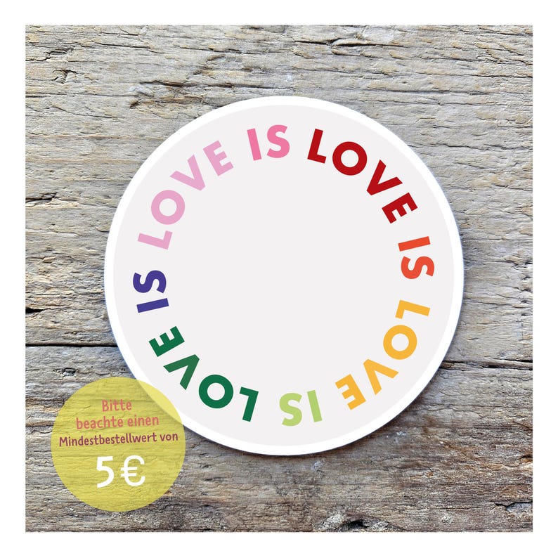 May include: A round white sticker with the words "LOVE IS LOVE" in a rainbow of colors. The text is arranged in a circle. The sticker is on a wooden surface.