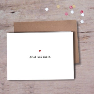 Può includere: Un biglietto bianco con un cuore rosso e il testo "Jetzt und immer." stampato in nero.