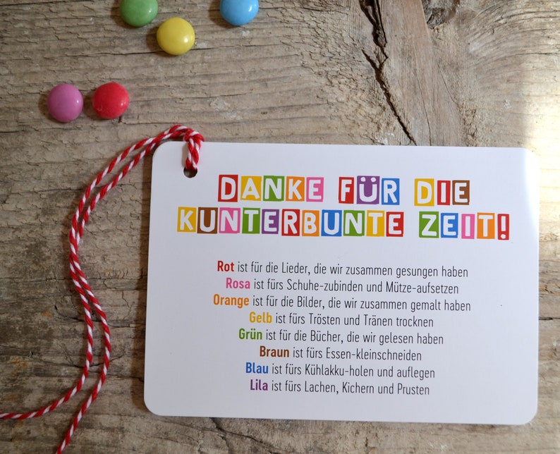 May include: A colorful card with the text "DANKE F&Uuml;R DIE KUNTERBUNTE ZEIT!" and a description of what each color represents. The card is tied with a red and white string.