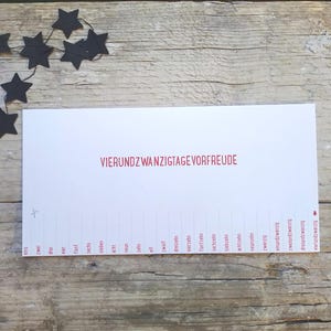 May include: A white rectangular paper strip featuring the red text VIERUNDZWANZIGTAGE VORFREUDE. Below, a sequence of numbers from eins to vierundzwanzig is printed with dashed lines for cutting, accompanied by a small scissor icon and a tree icon.
