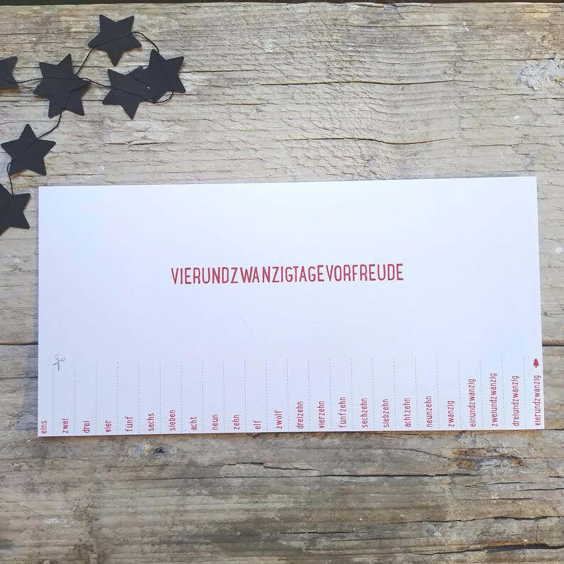 May include: A white rectangular paper strip featuring the red text VIERUNDZWANZIGTAGE VORFREUDE. Below, a sequence of numbers from eins to vierundzwanzig is printed with dashed lines for cutting, accompanied by a small scissor icon and a tree icon.