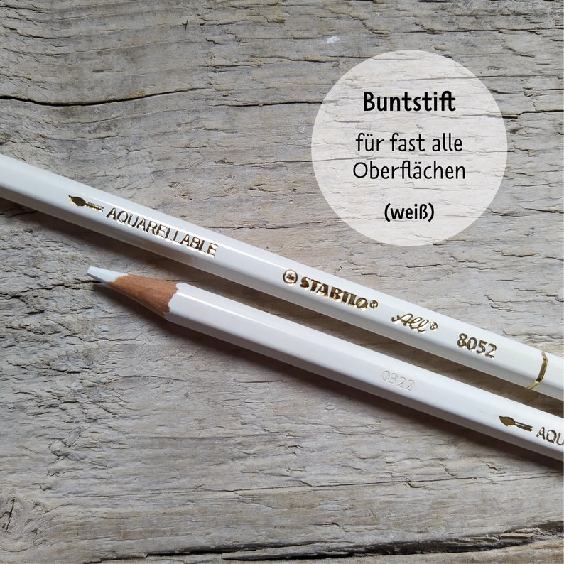 May include: White watercolor pencil with gold lettering that reads "STABILO All 8052 AQUARELLABLE". The pencil is on a light brown wooden surface. The text "Buntstif f&uuml;r fast alle Oberfl&auml;chen (wei&szlig;)" is visible in a circle above the pencil.