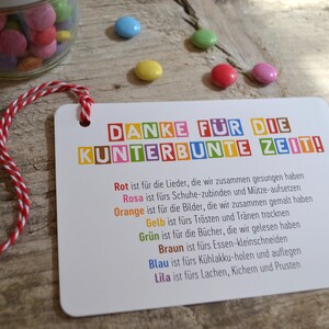 May include: A colorful card with the text "DANKE F&Uuml;R DIE KUNTERBUNTE ZEIT!" and a list of activities represented by different colors. The card is tied with a red and white string.