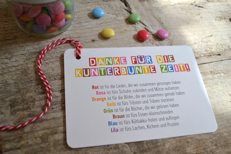 May include: A colorful card with the text "DANKE F&Uuml;R DIE KUNTERBUNTE ZEIT!" and a list of activities represented by different colors. The card is tied with a red and white string.
