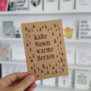 May include: A brown card with a white background and black text that reads "kalte Nasen warme Herzen" with a pattern of small black trees and stars.