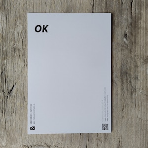 May include: White postcard with the word "OK" printed in black at the top. The bottom of the postcard has the text "GRATINHOF PAPETERIE" and a website address.