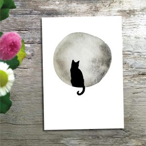 May include: A rectangular white print featuring a solid black silhouette of a cat sitting in front of a large, circular, watercolor-style moon rendered in shades of gray. The cat is positioned centrally, facing away, with its tail curved downward.