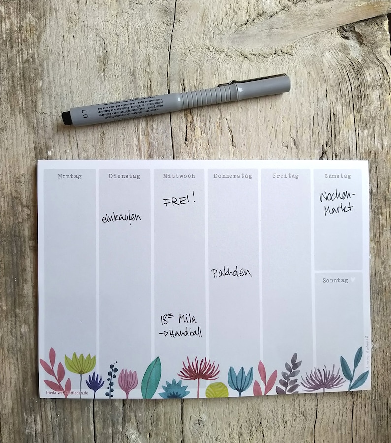 May include: A weekly planner with a grey background and a floral border. The days of the week are listed at the top: Monday, Tuesday, Wednesday, Thursday, Friday, Saturday, and Sunday. The planner has handwritten notes for each day, including "einkaufen", "FREI!", "Pabhden", "Wochen-Markt", and "18: Mila - Handball".